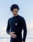 黒いウェットスーツを着た男性が海辺で立ち、手を胸元に当てている