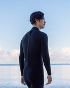 黒いウェットスーツを着た男性が海を見つめている
