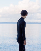 黒いウェットスーツを着た人物が海を見つめている