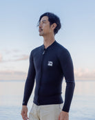 海辺で立つ男性が、黒い長袖ジャケットを着て、遠くを見つめている